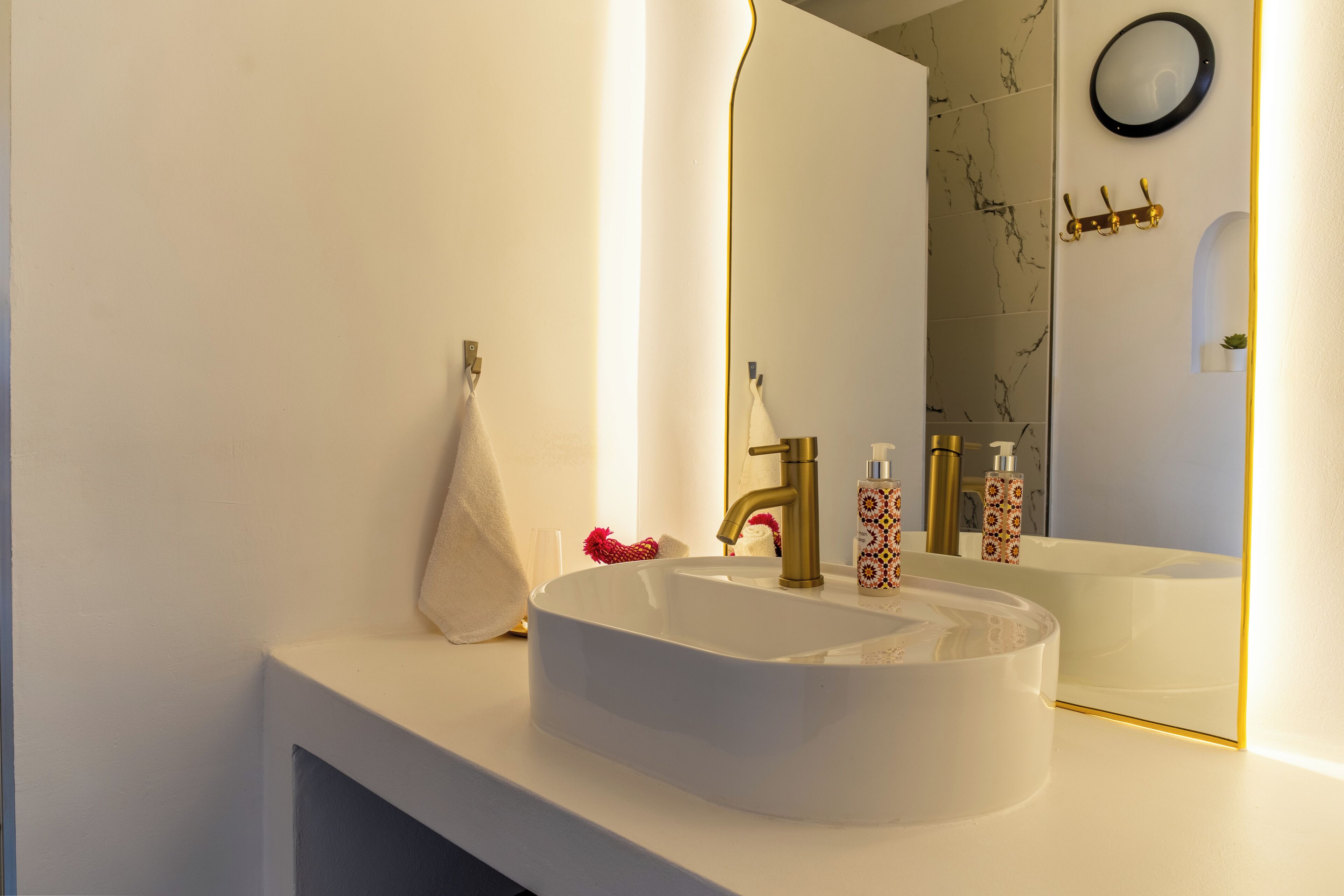 Une salle de bain avec un lavabo blanc, un robinet doré et un grand miroir avec un cadre doré.