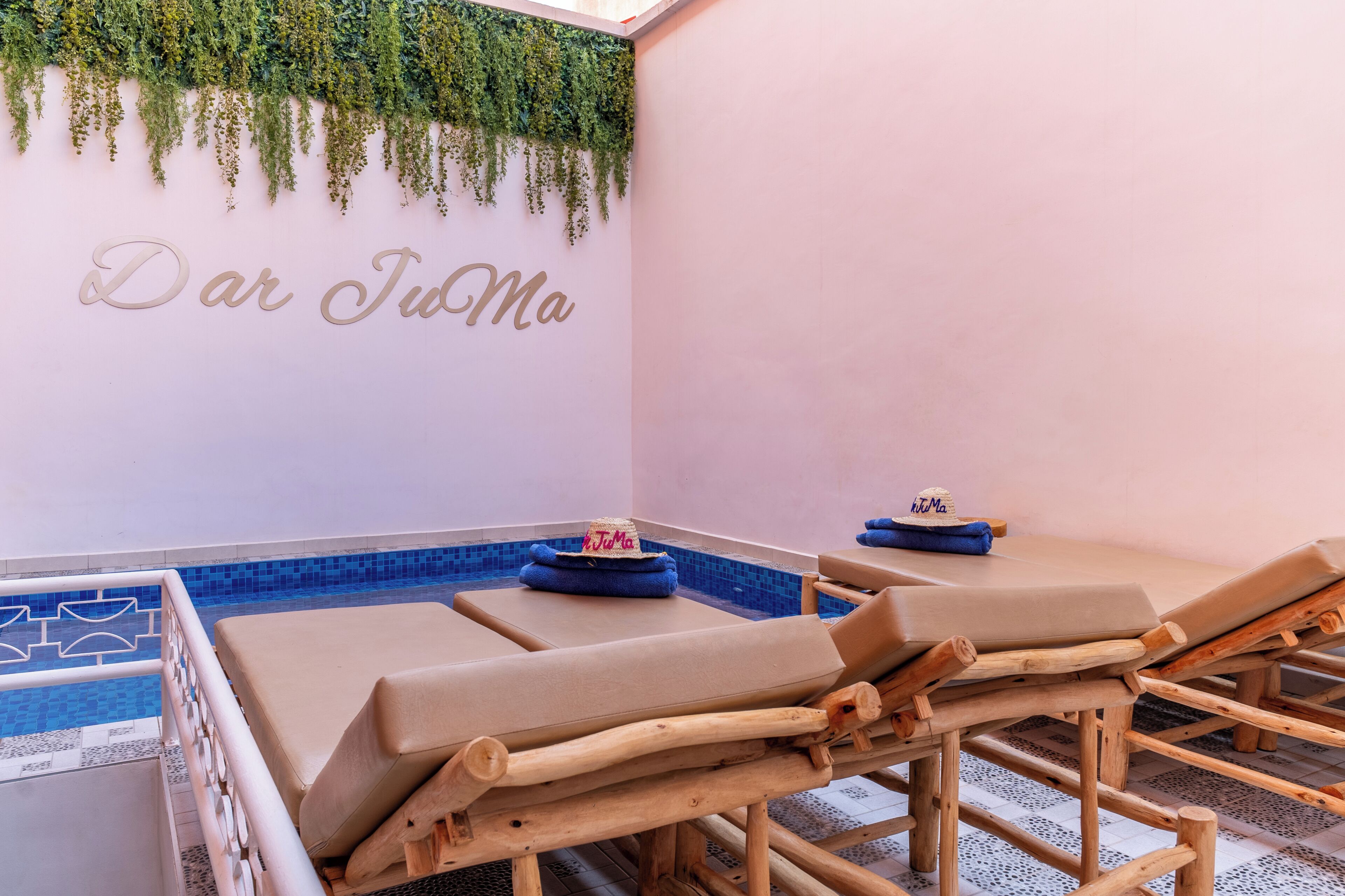 A spa area with wooden loungers, a small pool, and a wall with greenery and the text 'Dar JuMa'.