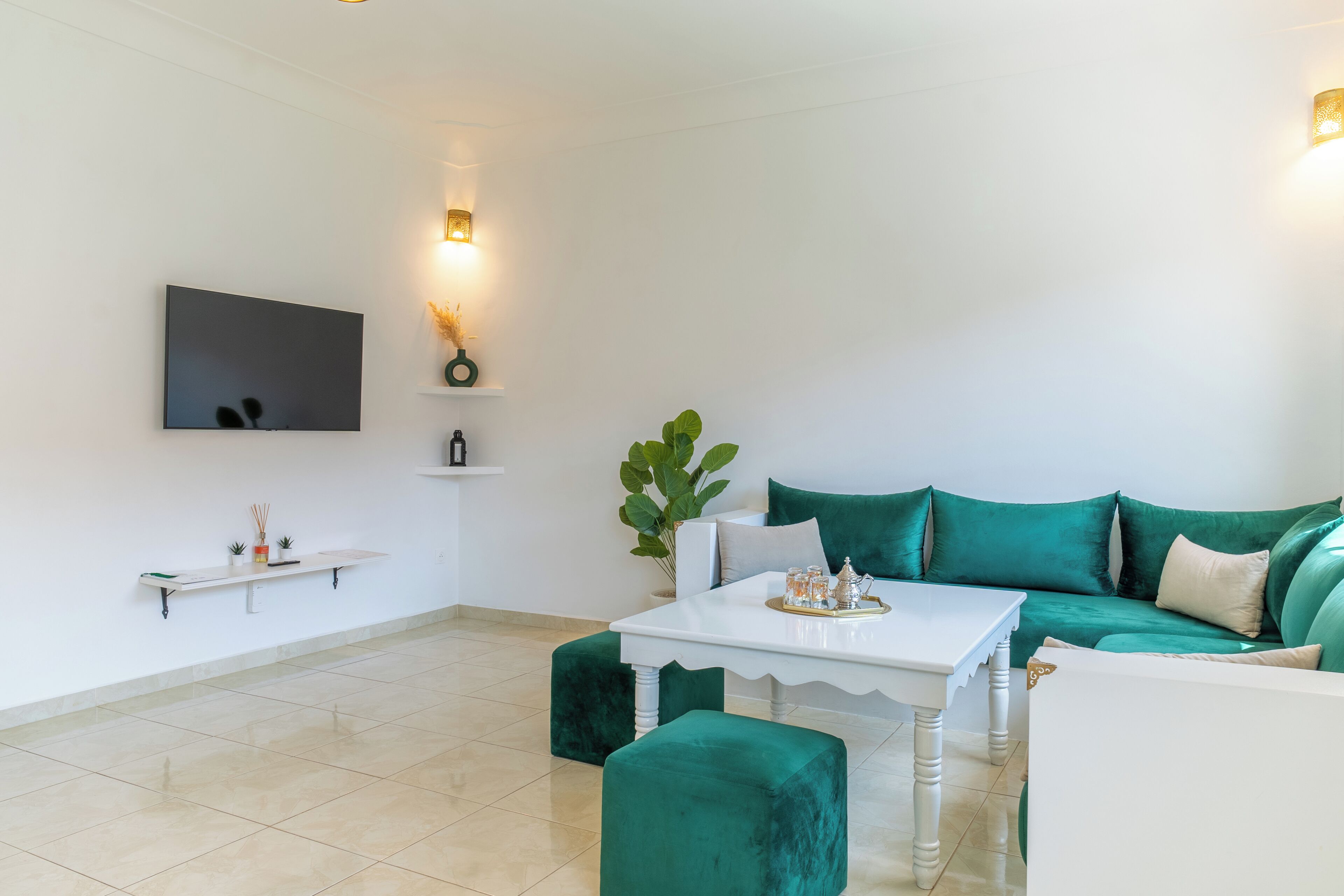 A modern living room with a white sofa, teal cushions, a white coffee table, and a flat-screen TV mounted on the wall.