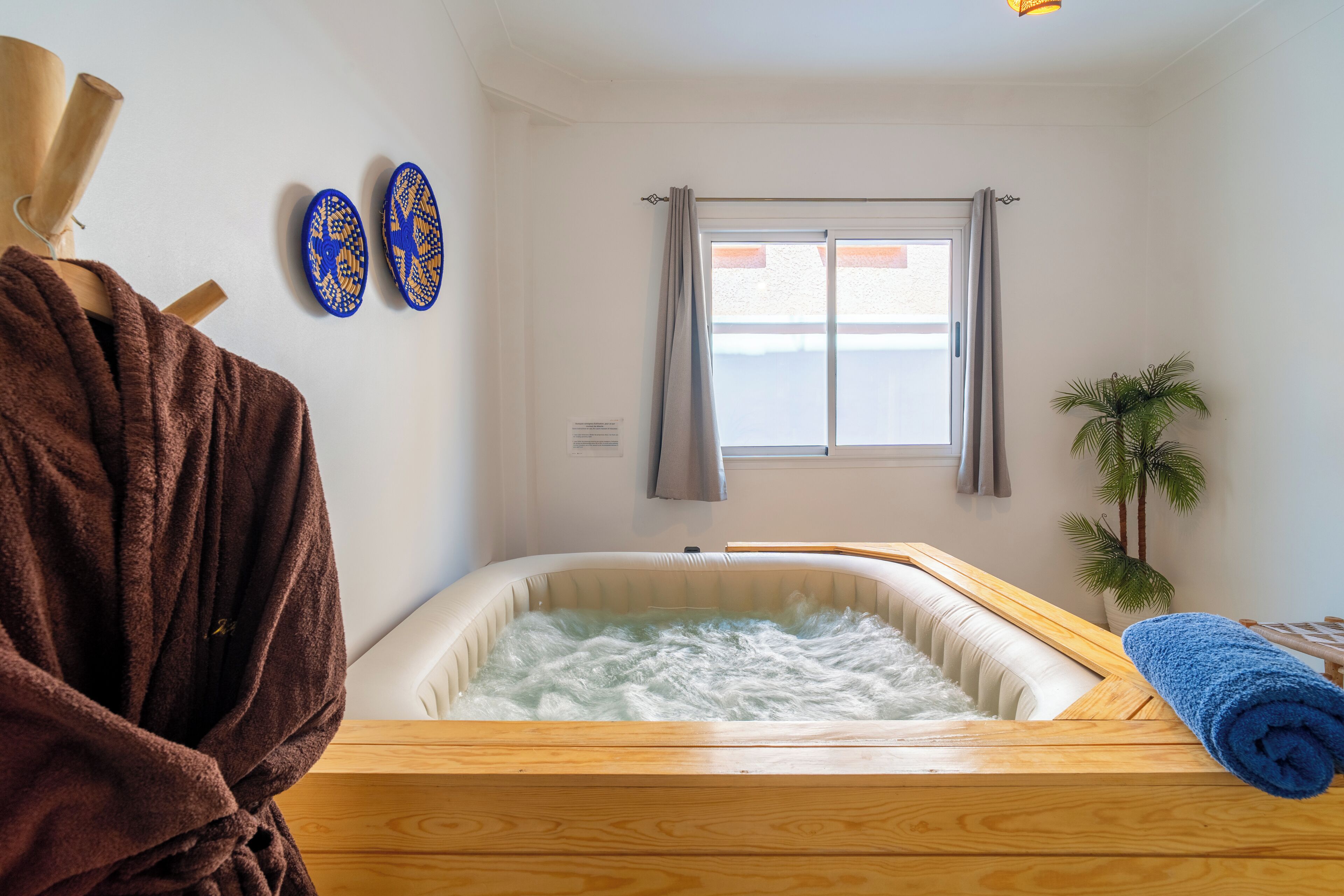 A room with a wooden bathtub, a towel, a small plant, and a window with curtains.