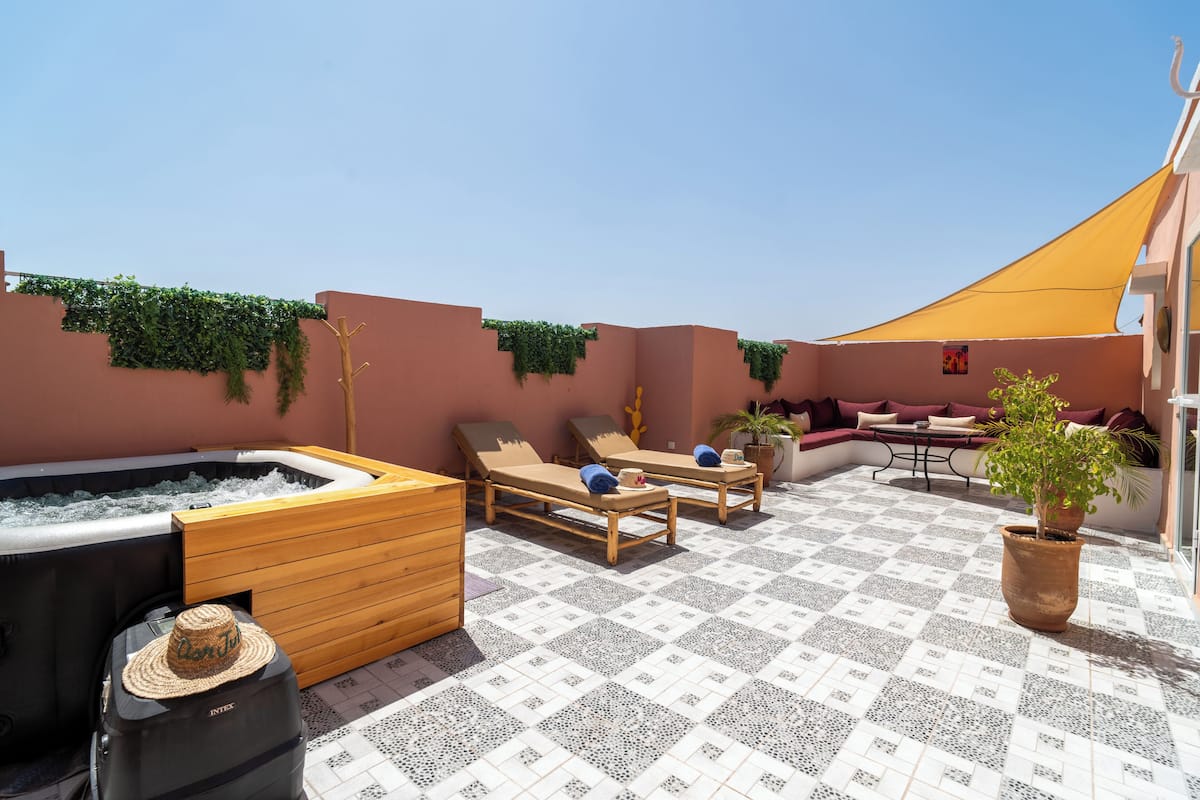 A rooftop terrace with a hot tub, lounge chairs, a wooden bench, and a potted plant.