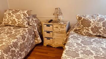 A bedroom with two beds, a nightstand with a lamp, and a small drawer unit.