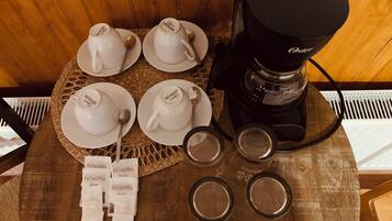 Una cafetera, cuatro tazas blancas y cuatro vasos vacíos sobre una mesa de madera.