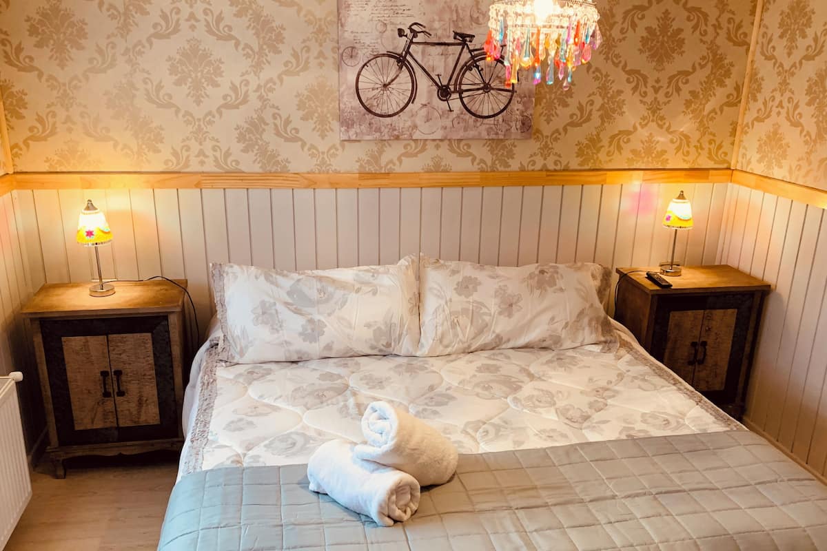 Un lit bien fait, avec une literie à motifs floraux, deux tables de chevet avec des lampes, une illustration de vélo accrochée au mur et une tête de lit en bois.