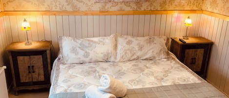 Un lit bien fait, avec une literie à motifs floraux, deux tables de chevet avec des lampes, une illustration de vélo accrochée au mur et une tête de lit en bois.