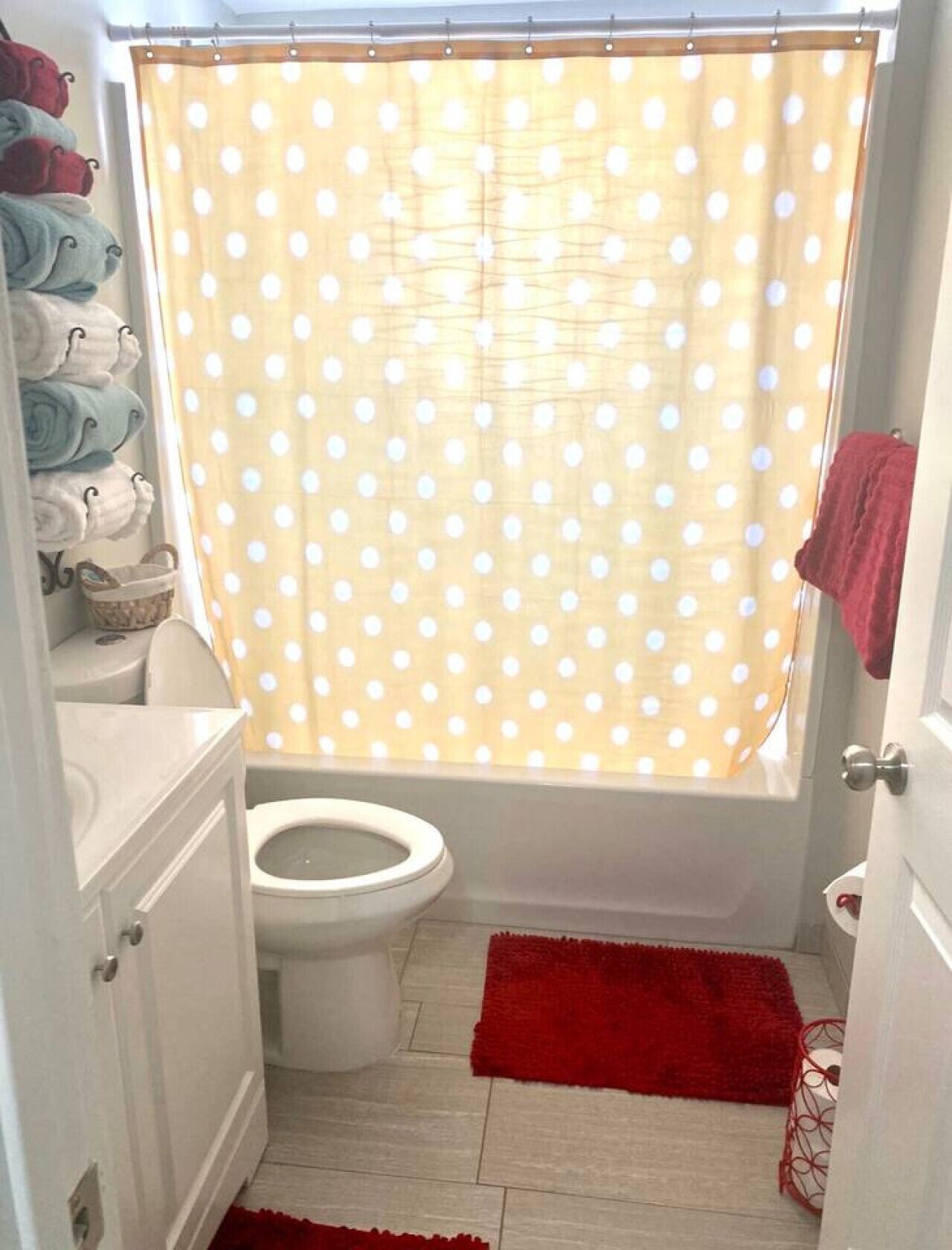 Een badkamer met een douchegordijn met stippen, een toilet, een rode mat en een handdoekrek met handdoeken.