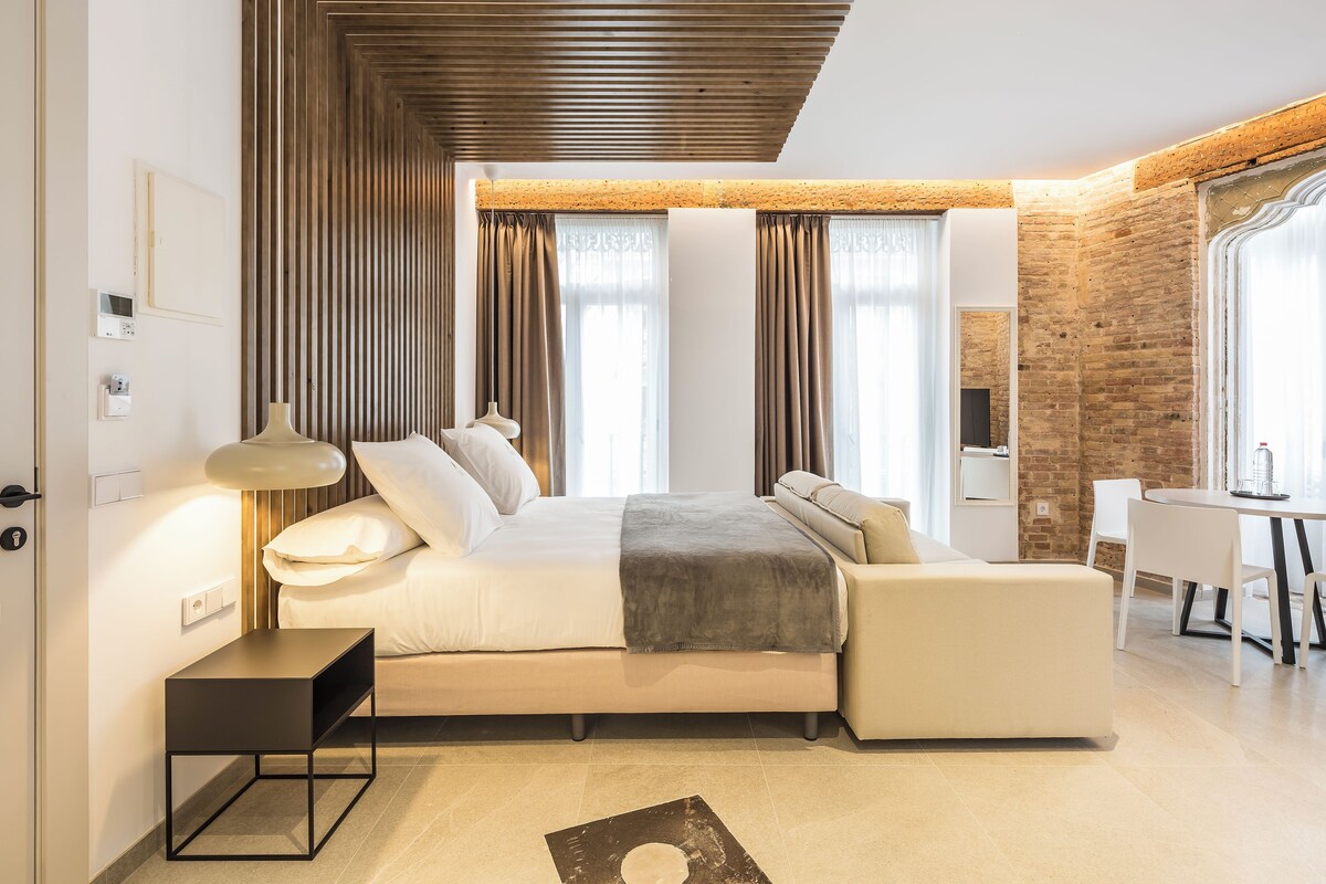 Une chambre moderne avec un lit, des tables de chevet, un bureau et un mur en briques.