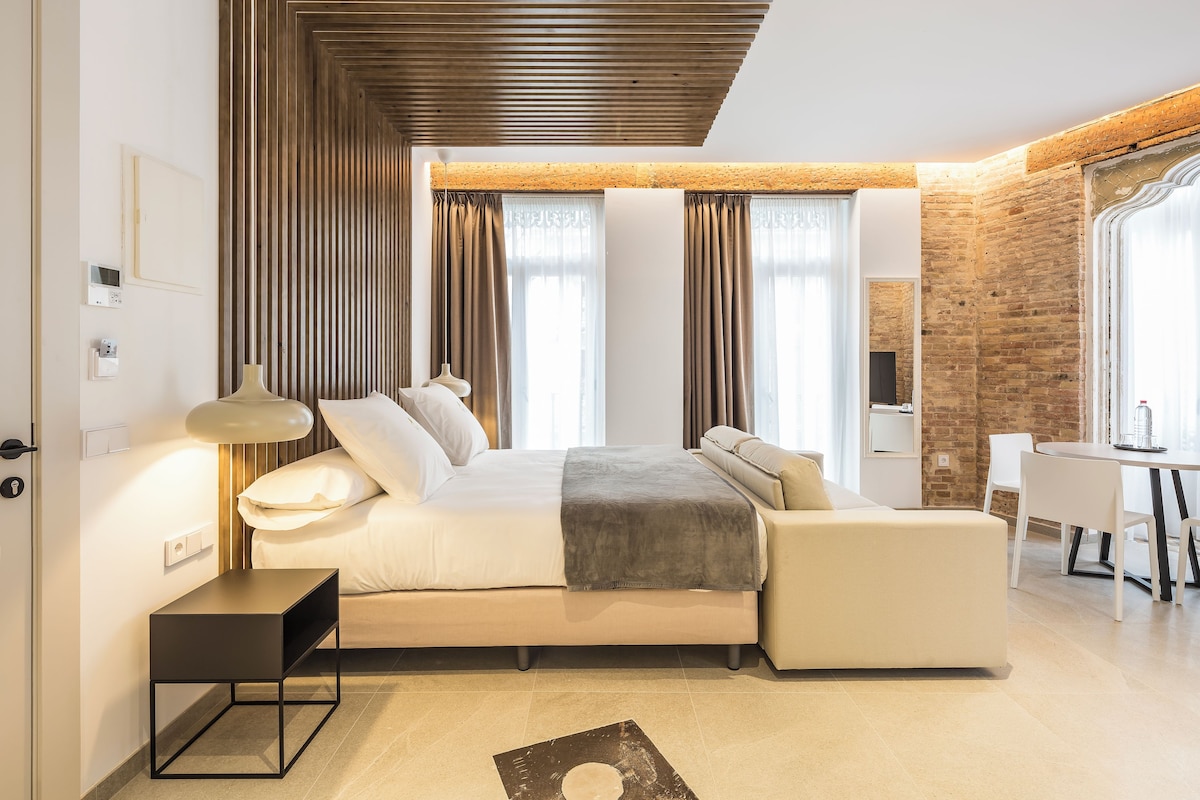 Un dormitorio moderno con cama, mesitas de noche, un escritorio y una pared de ladrillo.