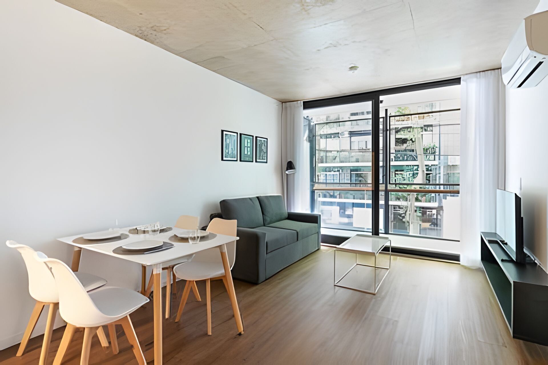 Een moderne woonkamer met een eetgedeelte, een grijze bank, houten vloeren en grote ramen met uitzicht op de stad.