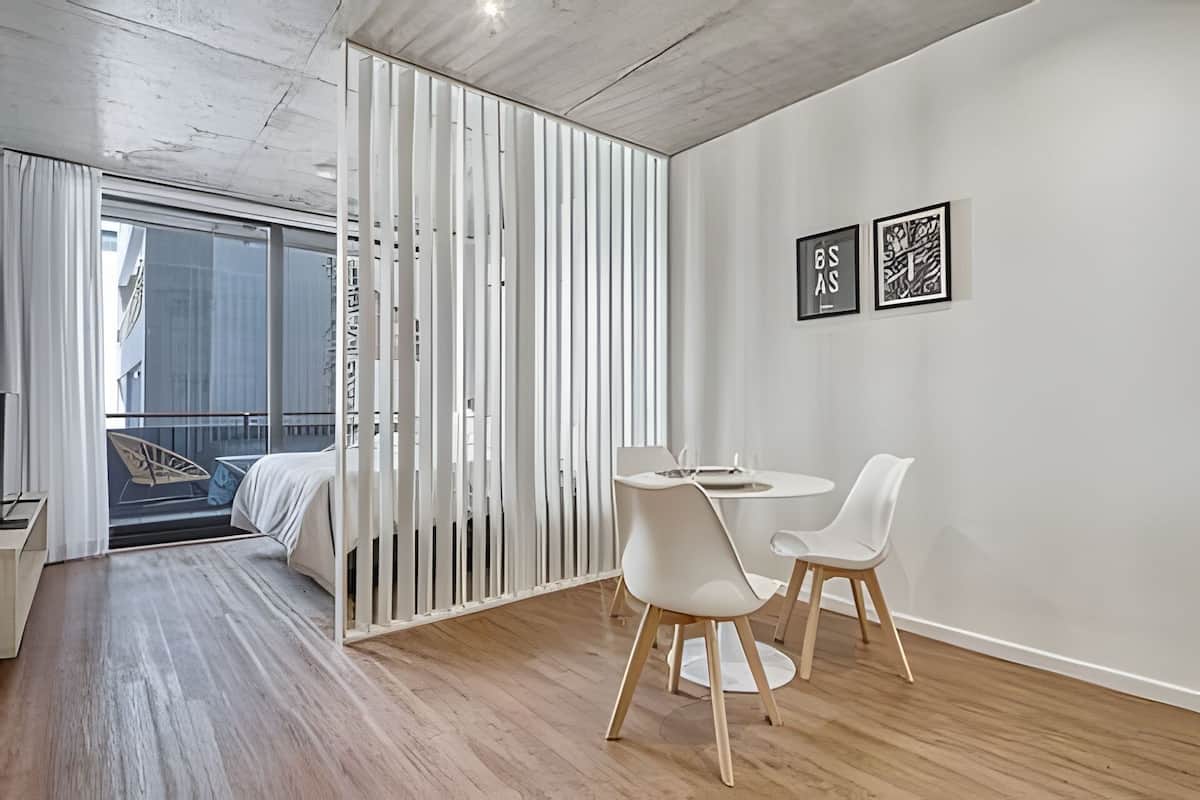 A modern room with a wooden floor, a bed, a balcony with a view, and two framed artworks on the wall.