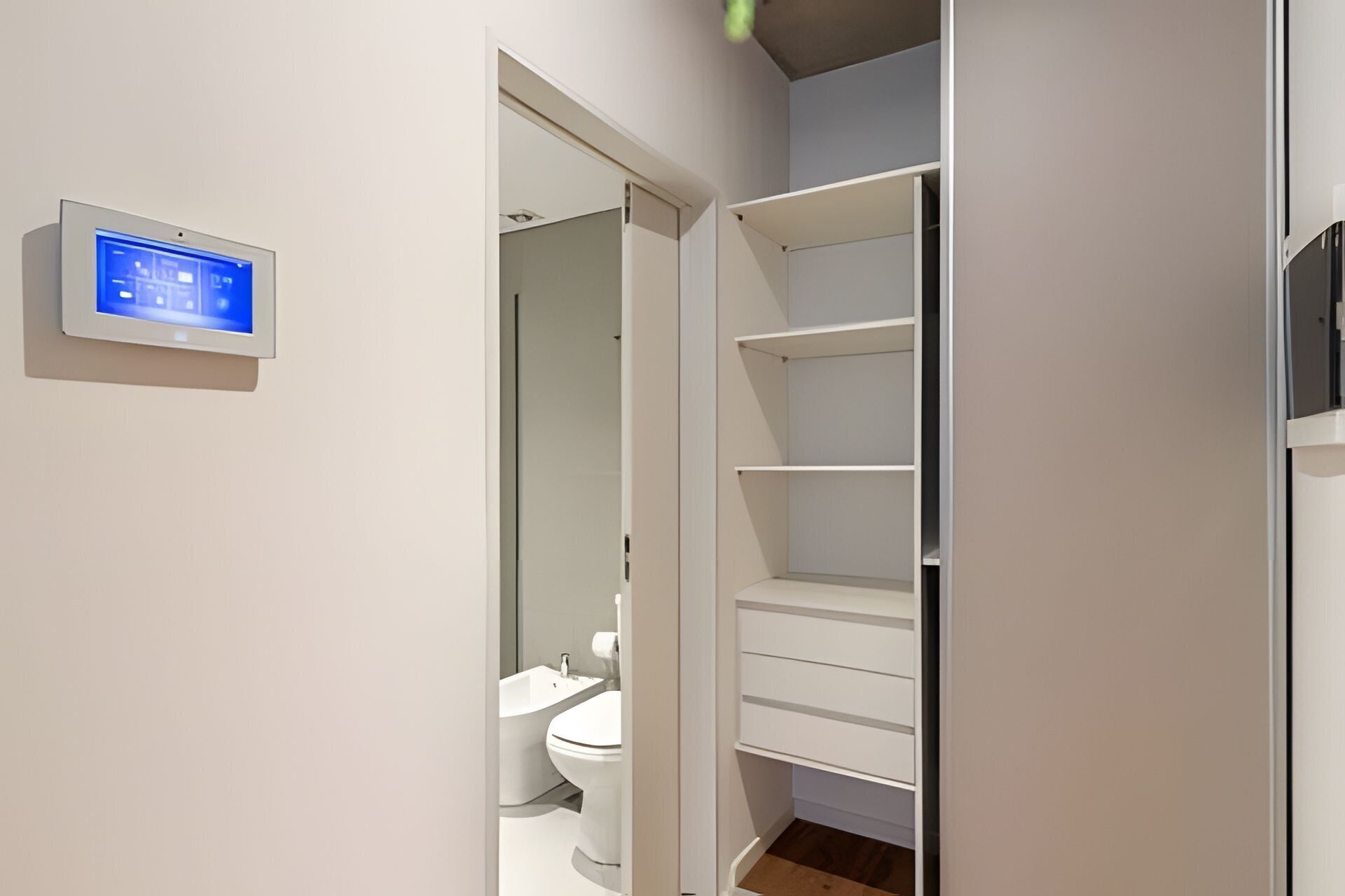 Un baño con inodoro, lavamanos y panel de control digital en la pared.