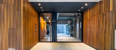 A modern building entrance with wooden paneling on the sides and a glass door leading to a parking garage.