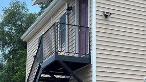 Una casa de dos pisos con una puerta roja, un portón de garaje y una escalera de metal negra que conduce al segundo piso.