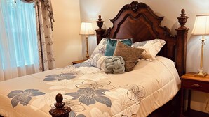 Una cama bien tendida con ropa de cama floral, cabecera de madera y dos mesitas de noche con lámparas.