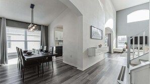 Ein modernes Interieur mit Essbereich, Küche und Wohnbereich, inklusive Treppe und großen Fenstern.