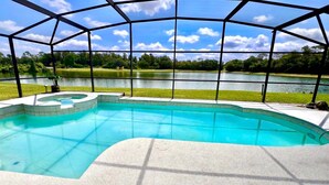 Ein geschwungenes Schwimmbecken, umgeben von einer überdachten Terrasse mit Blick auf einen See und Bäume.