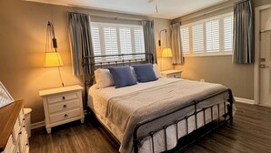 Quarto com cama, duas mesas de cabeceira, ventilador de teto e janela com cortinas.