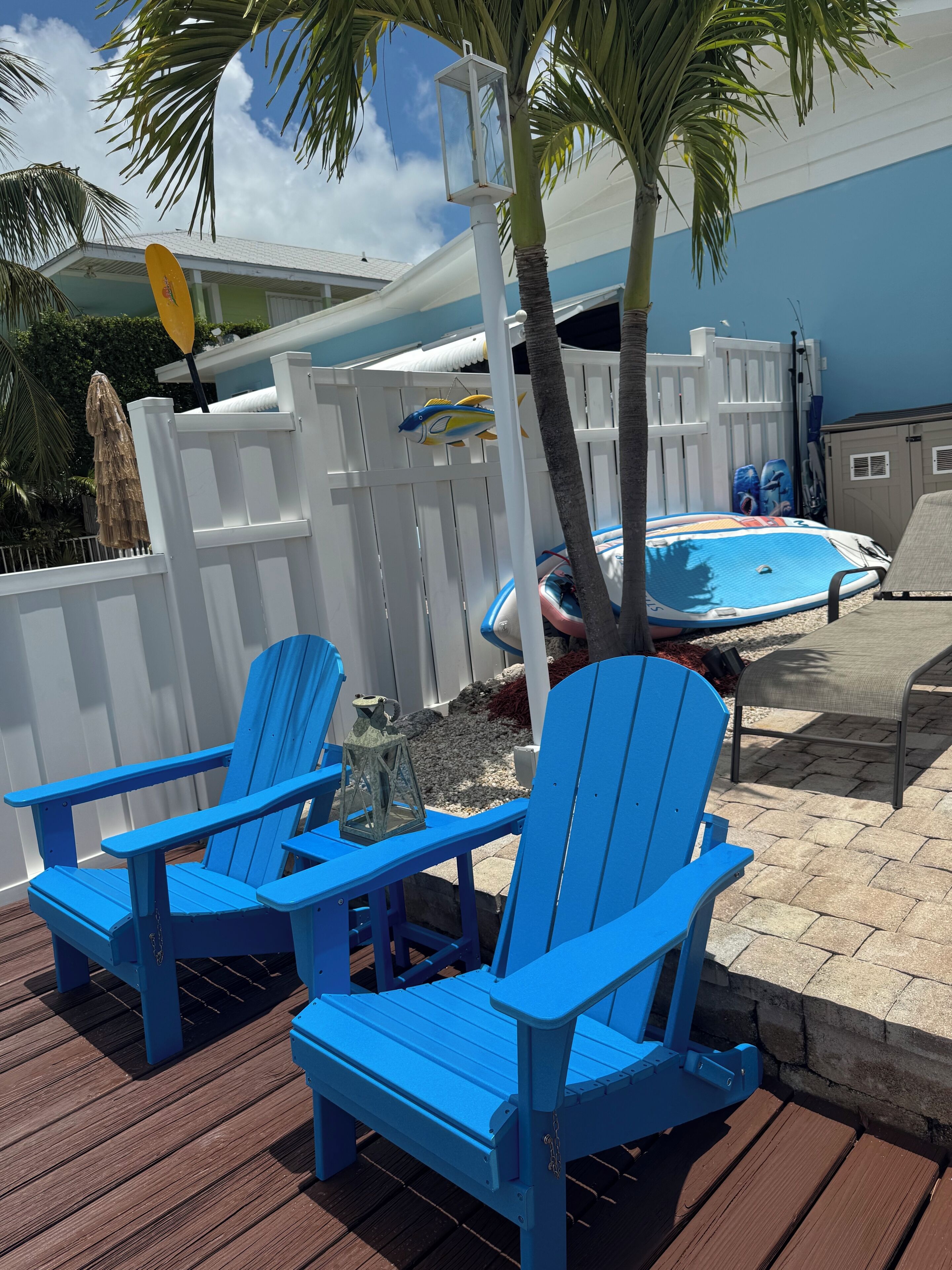 Une terrasse avec des chaises Adirondack bleues, une clôture blanche et un espace piscine.