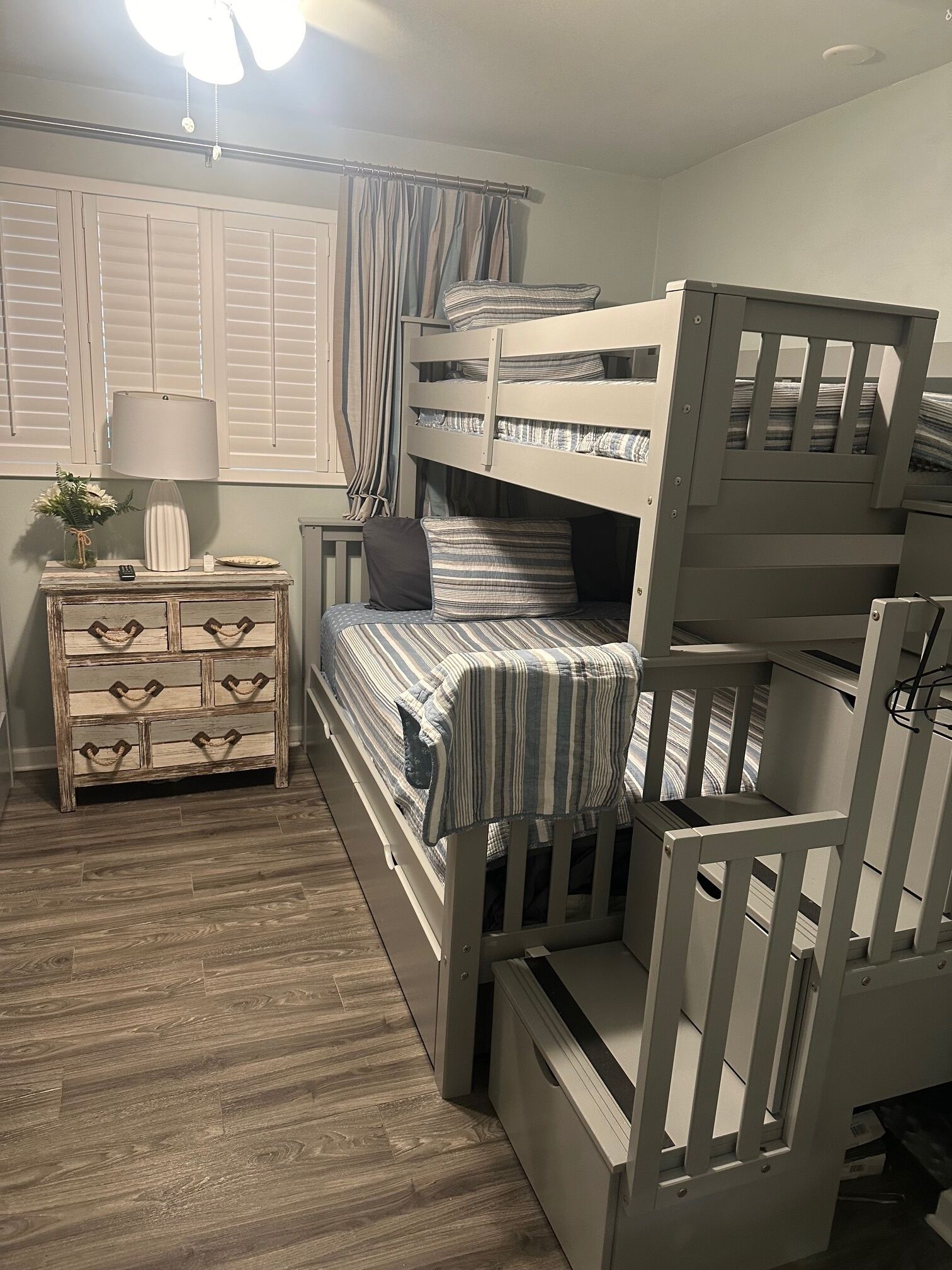 A bunk bed room with a wooden dresser, a lamp, and a window with curtains.