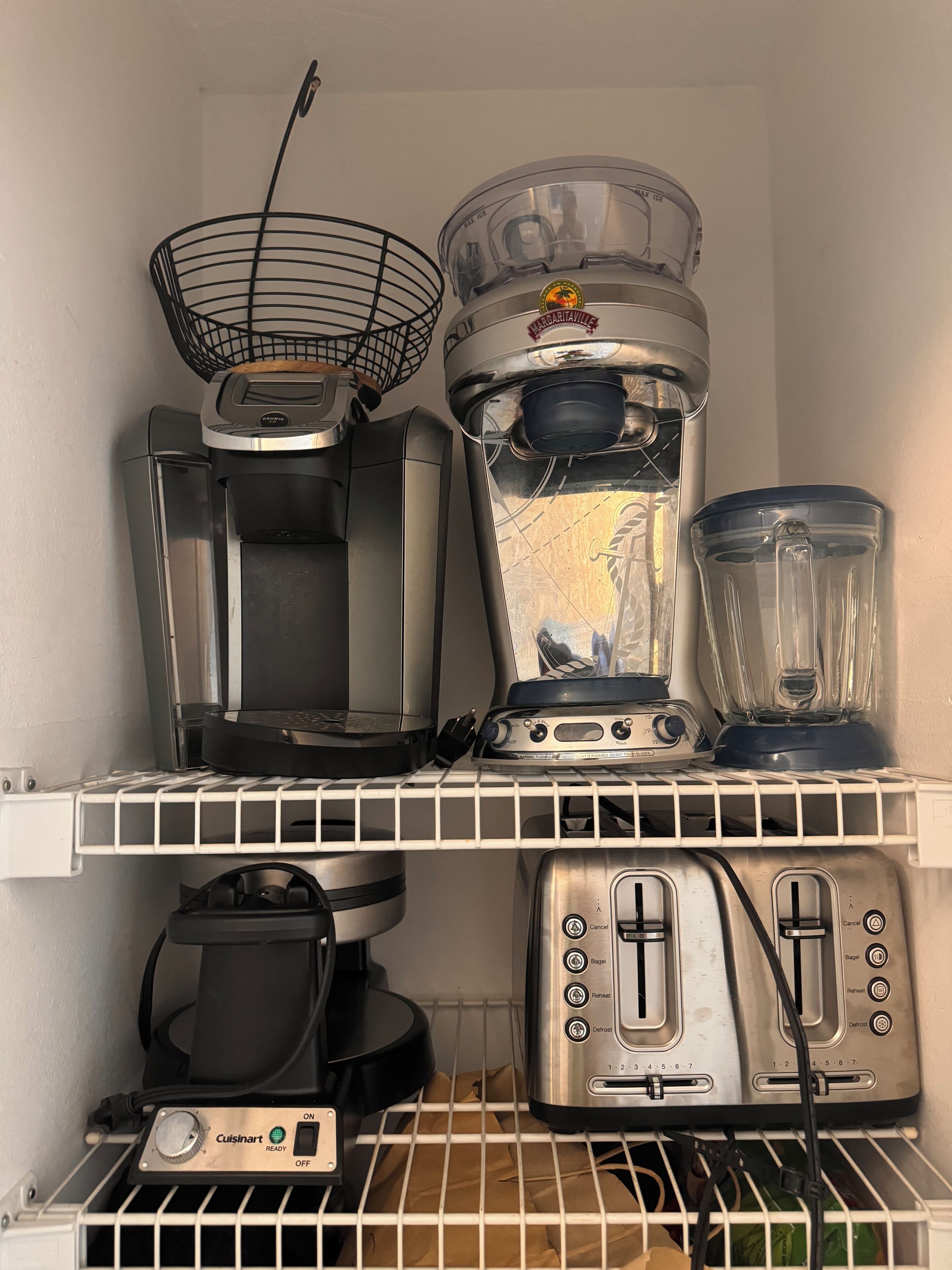 Une cuisine équipée d’une machine à café, d’un mixeur, d’un grille-pain et d’un robot culinaire Cuisinart, le tout rangé sur les étagères.