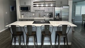 Cozinha moderna com uma ilha grande, eletrodomésticos de aço inoxidável e backsplash com ladrilhos em padrão herringbone.