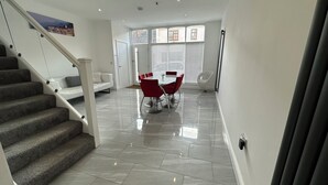 Ein modernes Interieur mit einer Treppe, einer Essecke mit roten Stühlen und Blick ins Freie durch große Fenster.