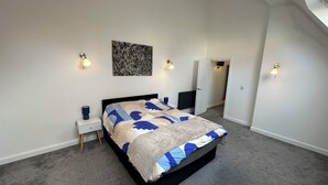 Ein Schlafzimmer mit einem Bett, einem Nachttisch, einer Wandleuchte und einer Tür zu einem anderen Raum.