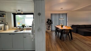 Eine moderne Küche mit weißen Schränken, ein Essbereich mit einem Holztisch und Stühlen, sowie eine Wand mit schwarz-weißen Streifen.