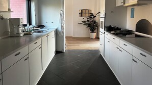 Eine moderne Küche mit weißen Schränken, einer Kaffeemaschine, einem Spülbecken und einem Herd. In der Mitte des Raumes steht ein Blumentopf.