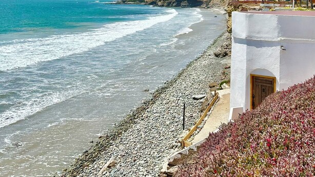 A coastal view with a rocky beach, a white building with a wooden door, and a clear blue sky. - SECLUDED One-of-a-Kind beachfront bungalow!  (Playas De Rosarito, B.C.)