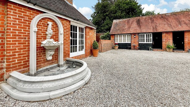 A brick building with a gravel courtyard, a fountain, and a chimney. - 1 bedroom accommodation in East Tytherley (East Tytherley)