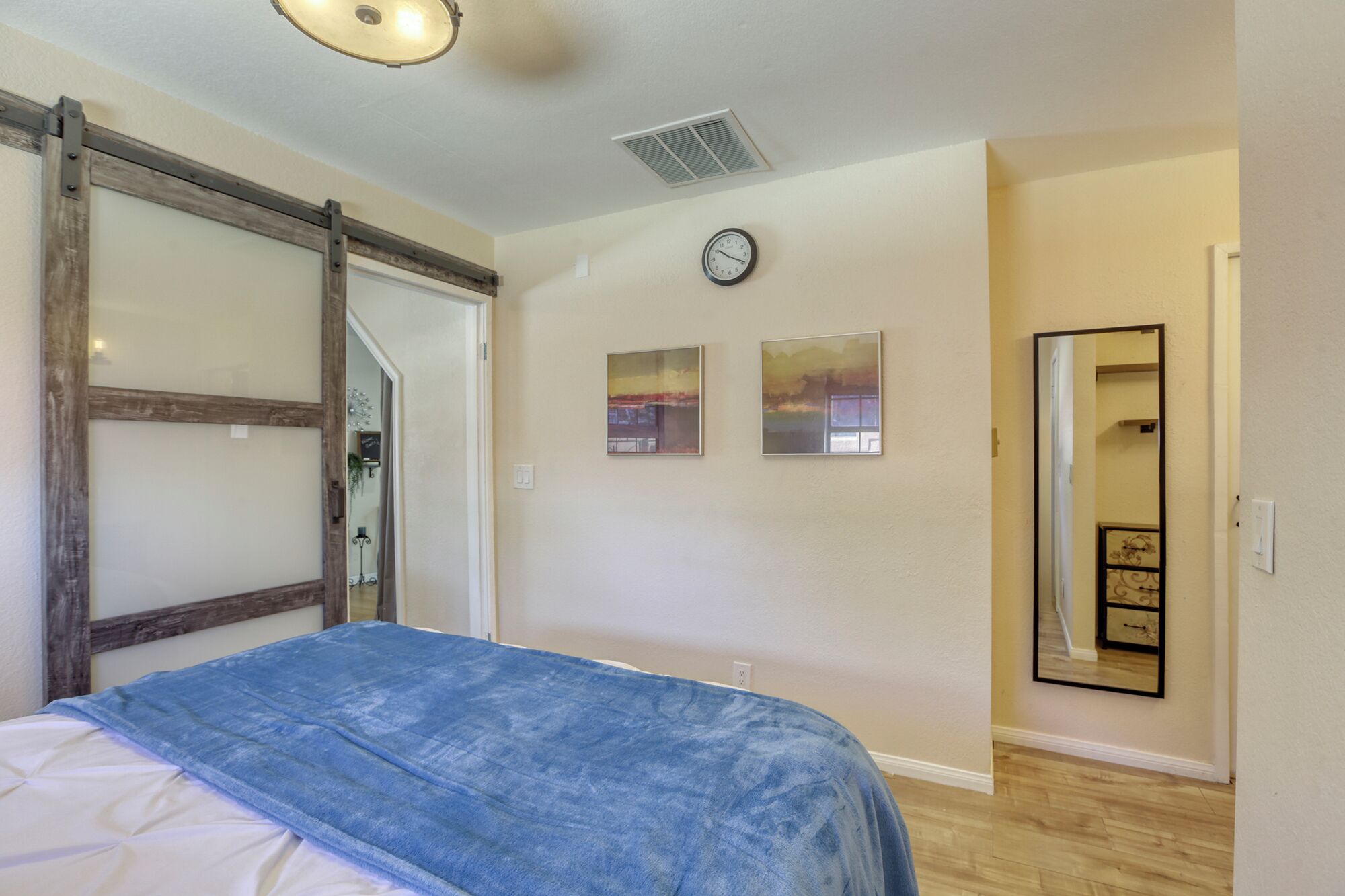 A bedroom with a bed, a clock, and two framed pictures on the wall.