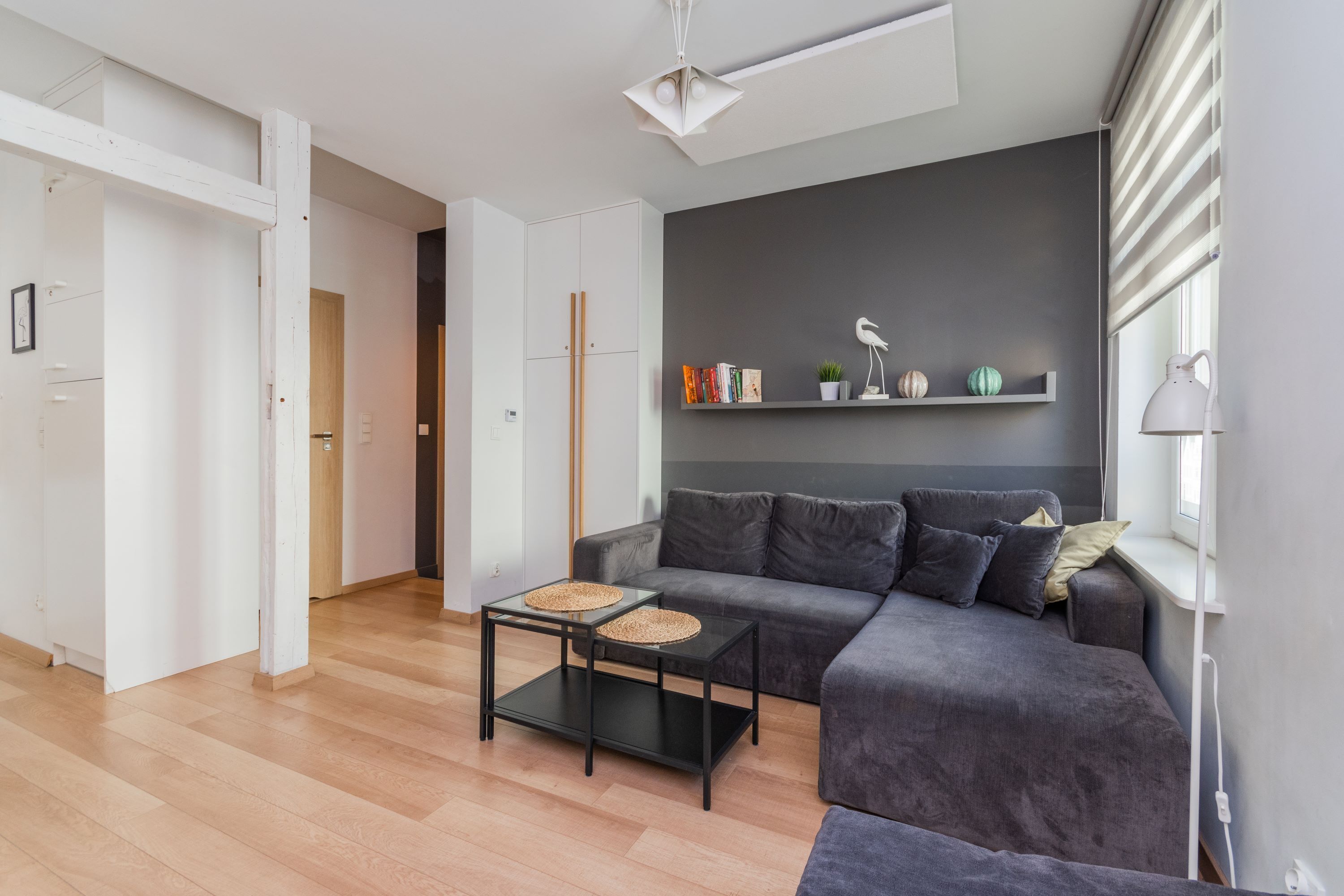 A modern living room with a grey sofa, a black coffee table with woven placemats, and a bookshelf with decorative items.