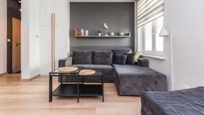 Una sala de estar moderna con un sofá gris, una mesa de centro de vidrio y una estantería con adornos.