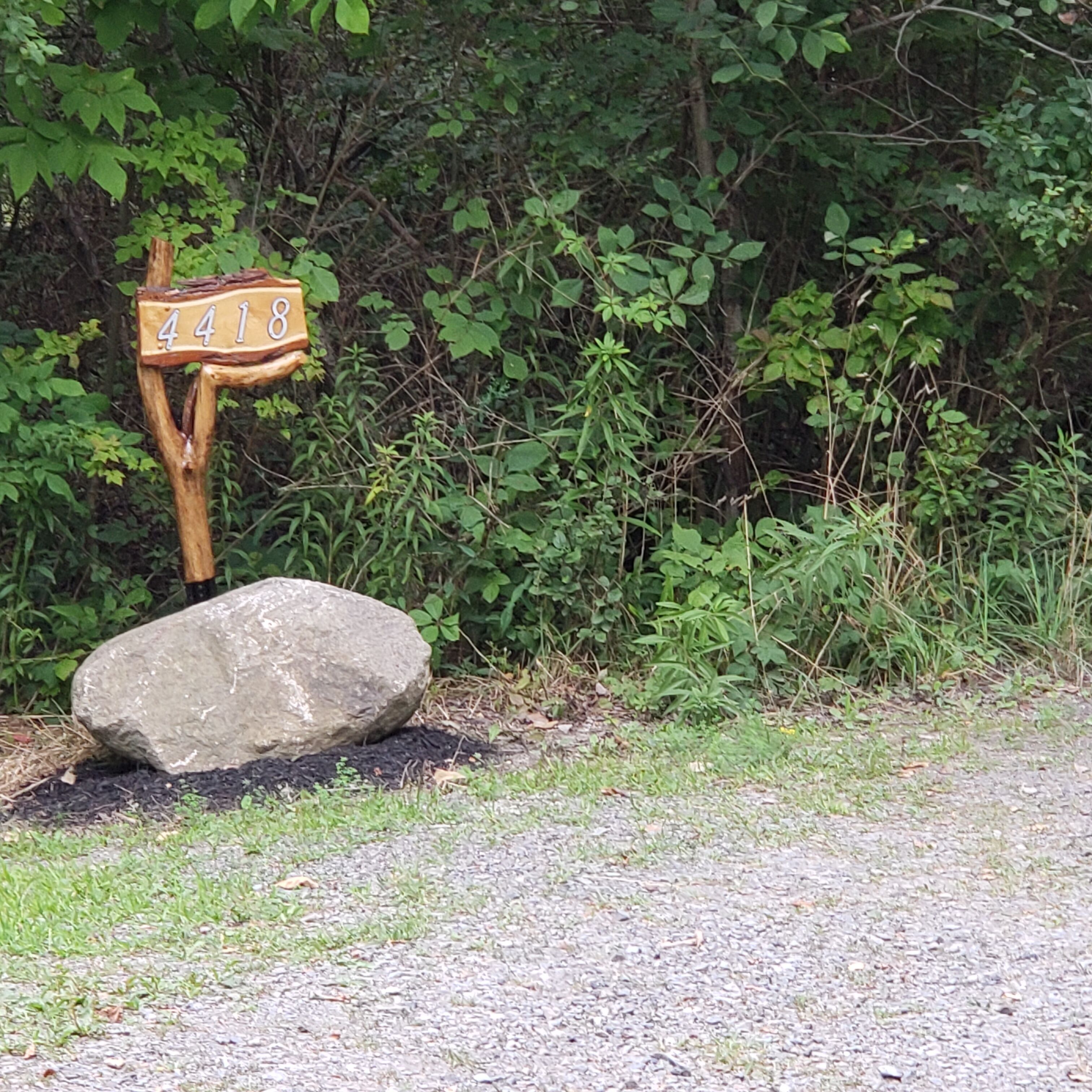 Ein Holzschild mit der Nummer 4418, ein großer Felsen und üppiges Grün im Hintergrund.