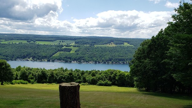 A wooden deck with a metal railing overlooking a lake and forested hills. - Paradise. Front deck. All comforts of home.  Great view. Serenity. (Keuka Park)