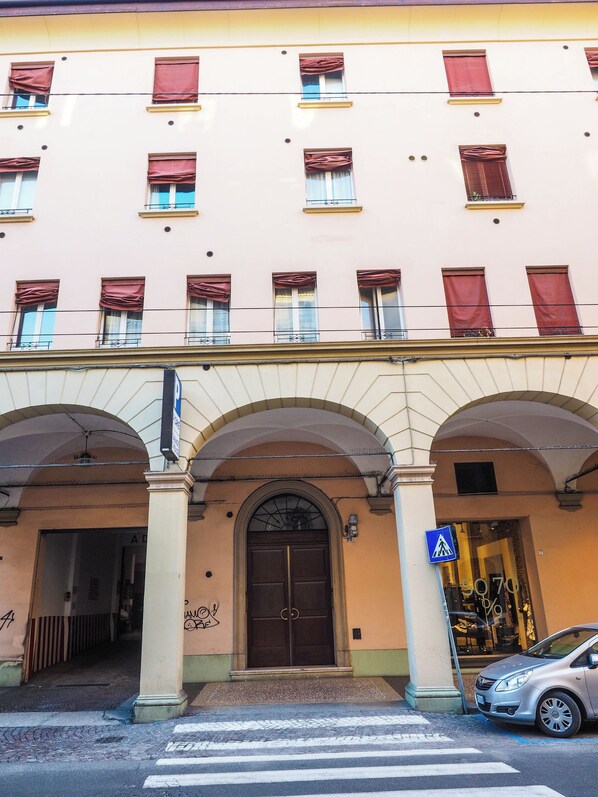 A building with a large arched entrance, multiple windows with red curtains, and a pedestrian crossing sign.
