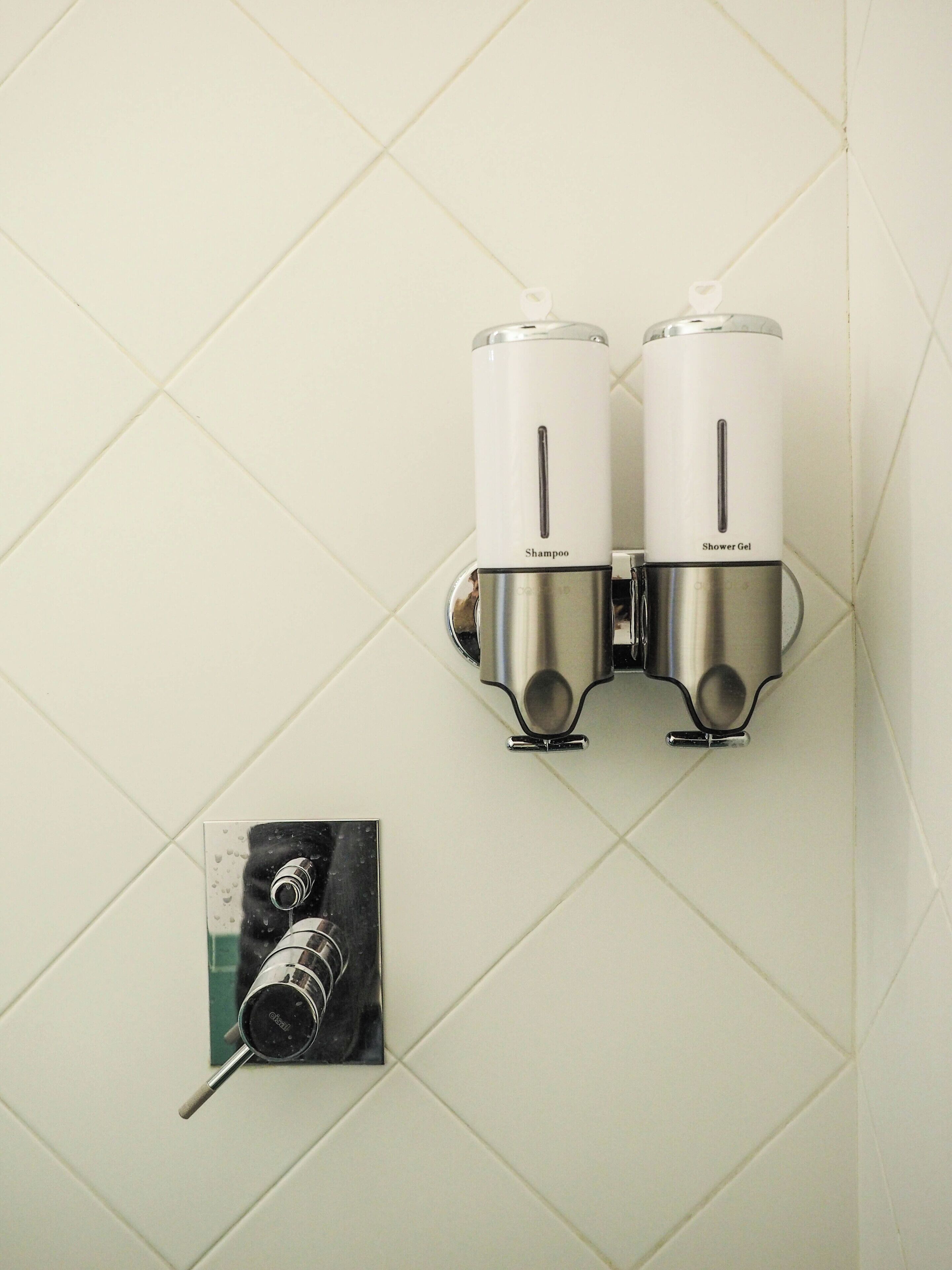 A wall-mounted shower system with two dispensers labeled "Shampoo" and "Shower Gel".
