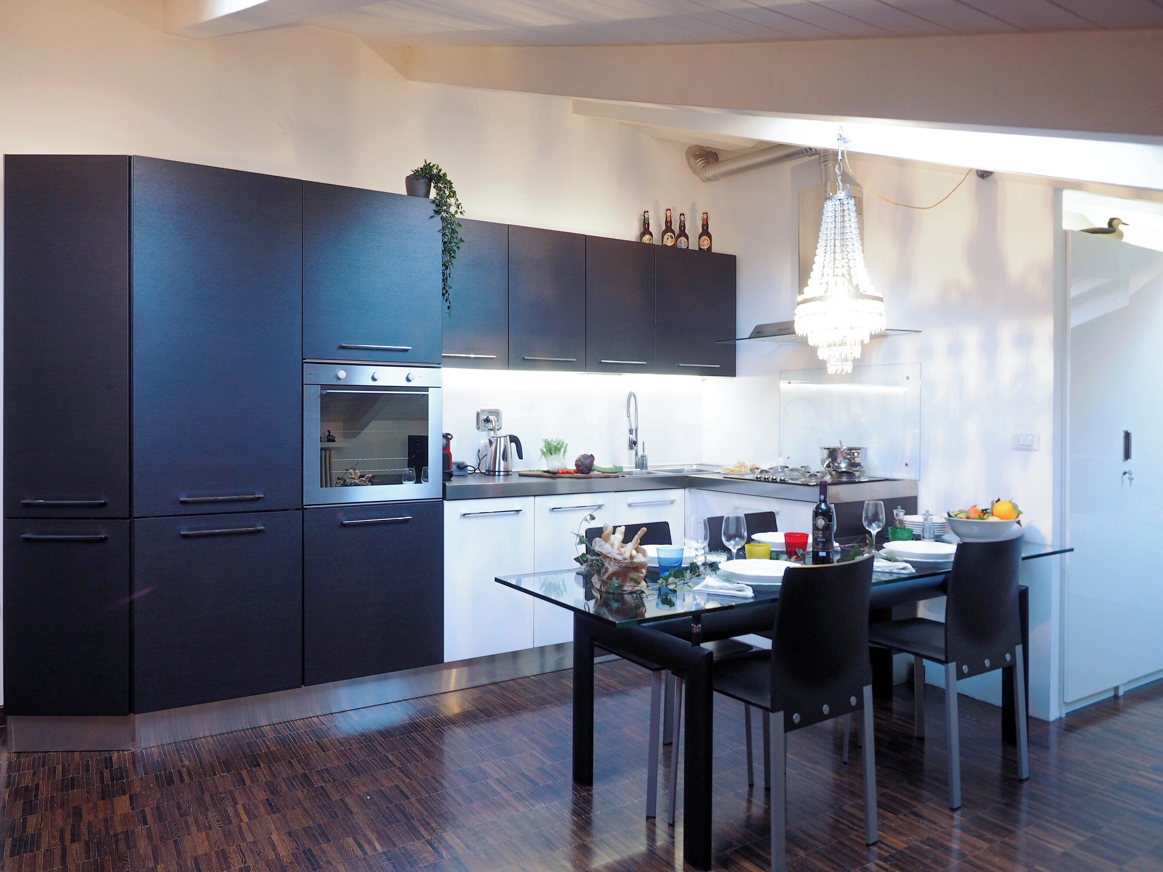 A modern kitchen with dark cabinets, stainless steel appliances, and a dining area with a glass table and chairs.