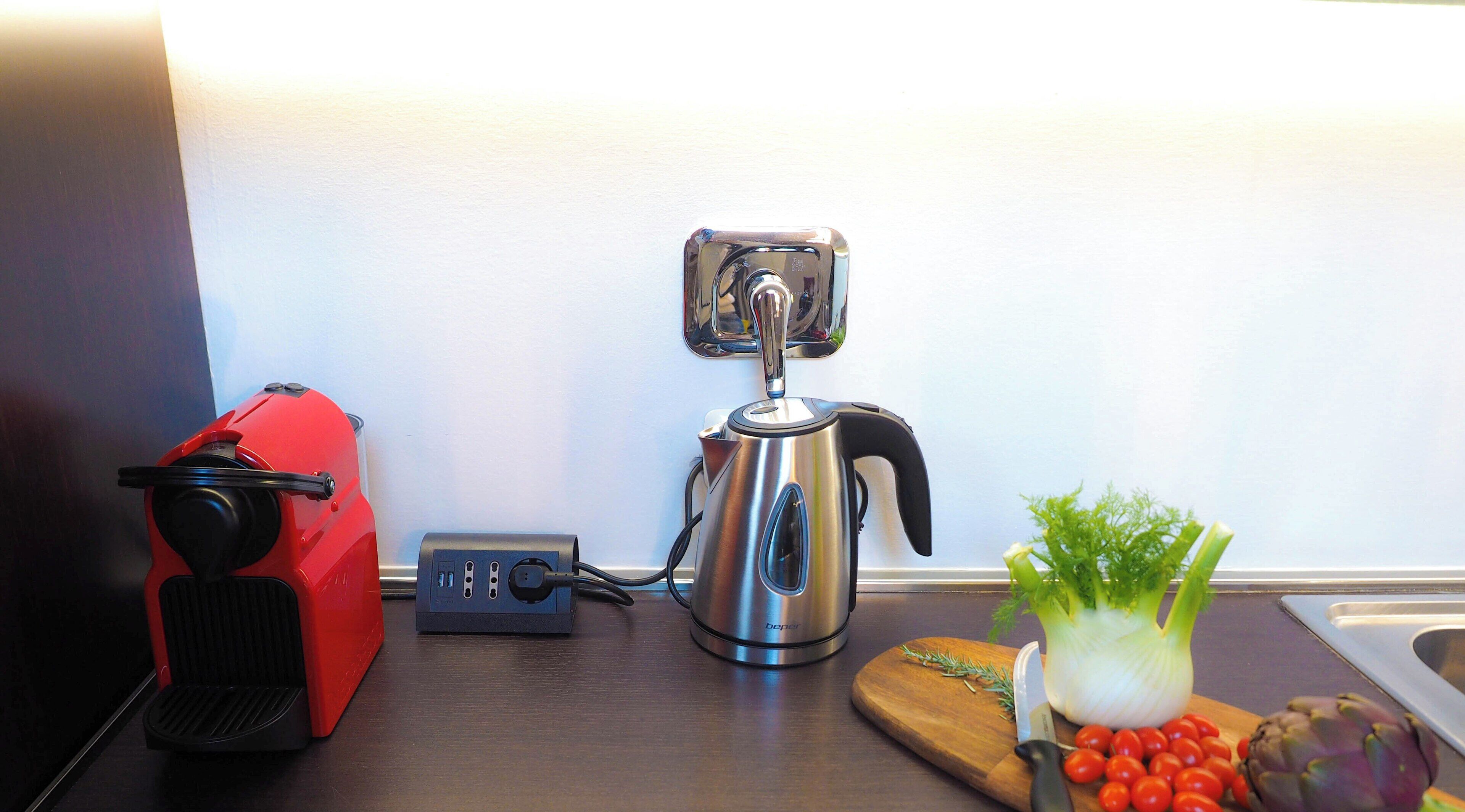A kitchen counter with a coffee maker, a red appliance, and fresh vegetables.