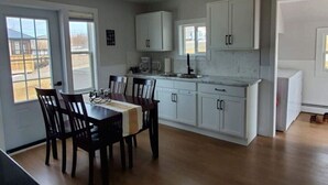 Een keuken met witte kasten, een eettafel met stoelen en een raam dat natuurlijk licht binnenlaat.