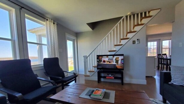 Een moderne woonkamer met een houten salontafel, zwarte fauteuils, een zwarte bank en een trap naar een hoger niveau.