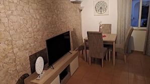 A living room with a stone wall, a flat-screen TV, a dining table with chairs, and a window with curtains.
