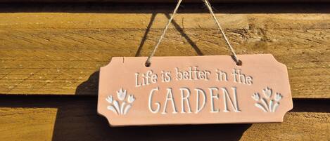 Ein Holzschild mit dem Schriftzug „Life is better in the GARDEN“ und dekorativen floralen Elementen.