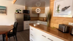 Una cocina moderna con armarios de madera, encimera de madera, una mesa de comedor con sillas, un microondas, un tostador y un refrigerador.