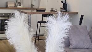 Una cocina moderna con armarios blancos, una cafetera y un comedor con un sofá gris.