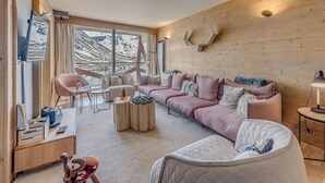 Una sala de estar moderna con una pared de madera, un sofá rosa, una mesa de centro redonda y una mesita de noche con una lámpara.