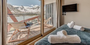 A hotel room with a large window offering a mountain view, a bed with two towels, a TV on the wall, and a chair by the window. - 200m from ski slopes, 4th floor, view lake, ski locker, 150m², Tignes (Tignes)