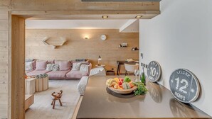 Una sala de estar moderna con techo de madera, un sofá rosa, una mesa redonda con fruta y decoración en la pared, incluyendo dos letreros con números.