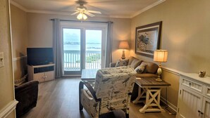 Un salon comprenant un canapé, un fauteuil, un téléviseur, une table et un balcon avec vue.